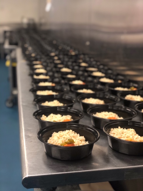 line of bowls with fresh prepared meals inside waiting to be packaged